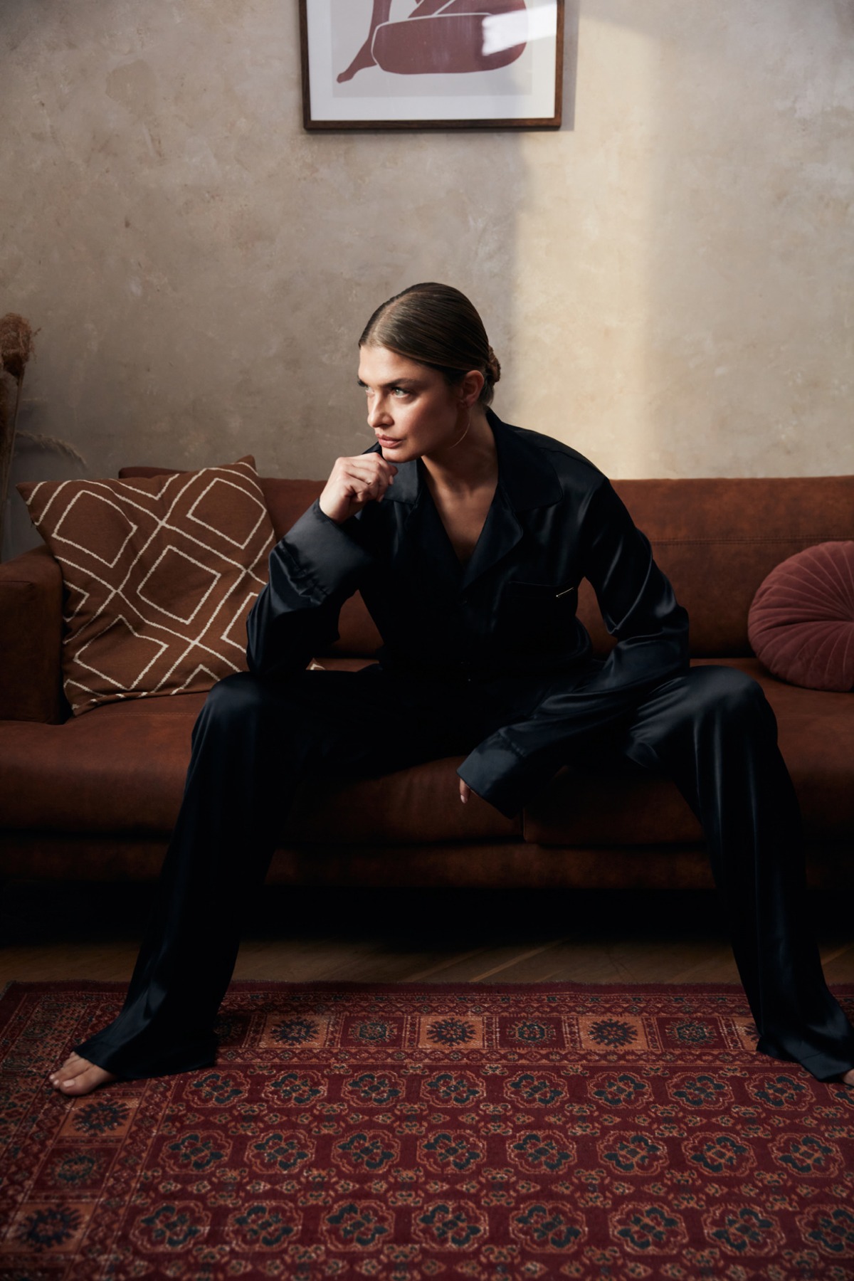 Bilquiis campaign: woman in a black tailored suit seated on a sofa